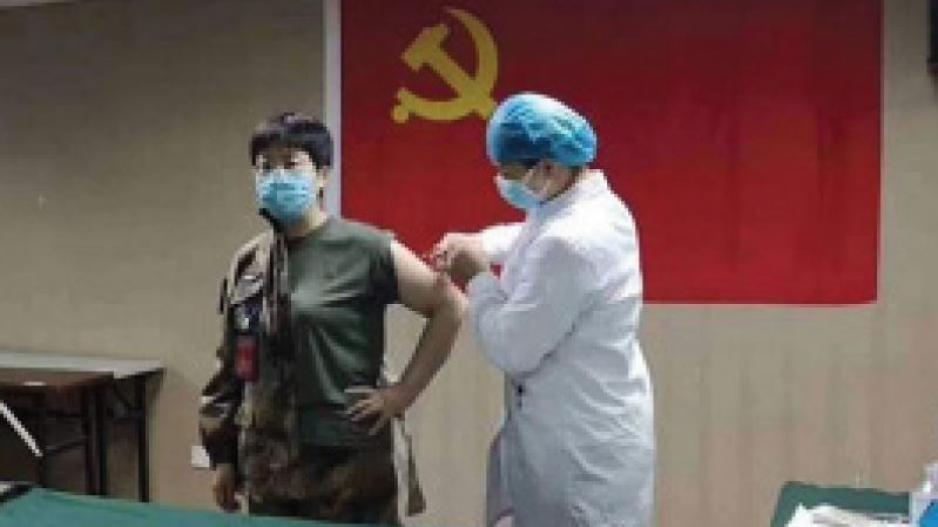 Çin'de ÇKP bayrağı önünde aşı denemesinde gönüllü olan bir Halk Kurtuluş Ordusu askeri doktoru